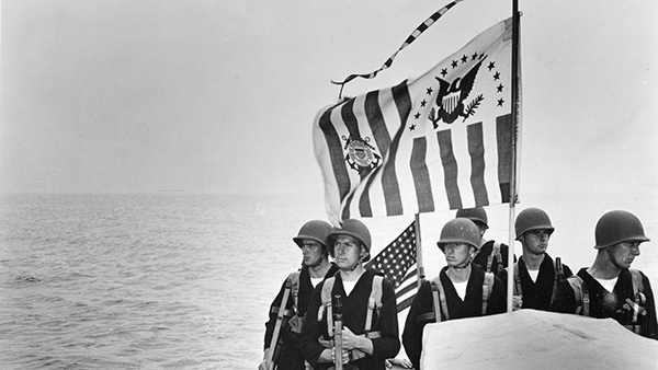 World War II Coast Guardsmen standing beneath the United States Coast Guard ensign